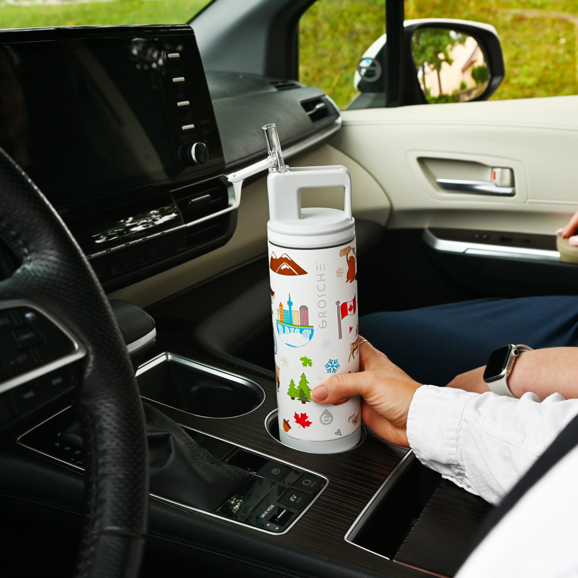 Person holding a white water bottle with colourful illustrations inside a car.