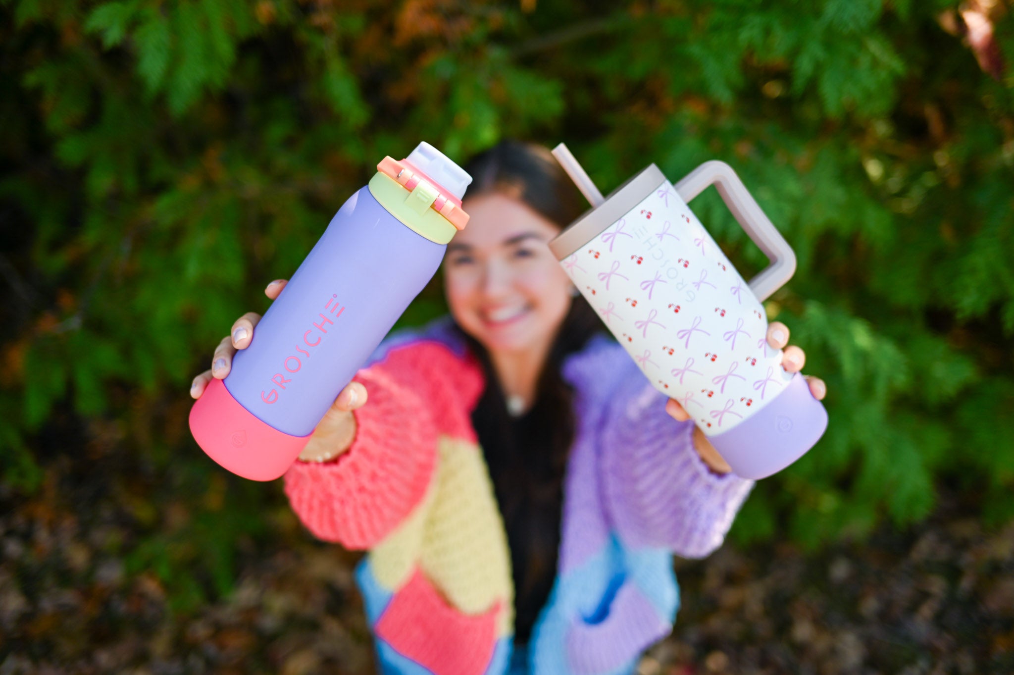 GROSCHE Kamloops and ASPEN Woman smiling and holding two colorful water bottles outdoors with greenery in the background