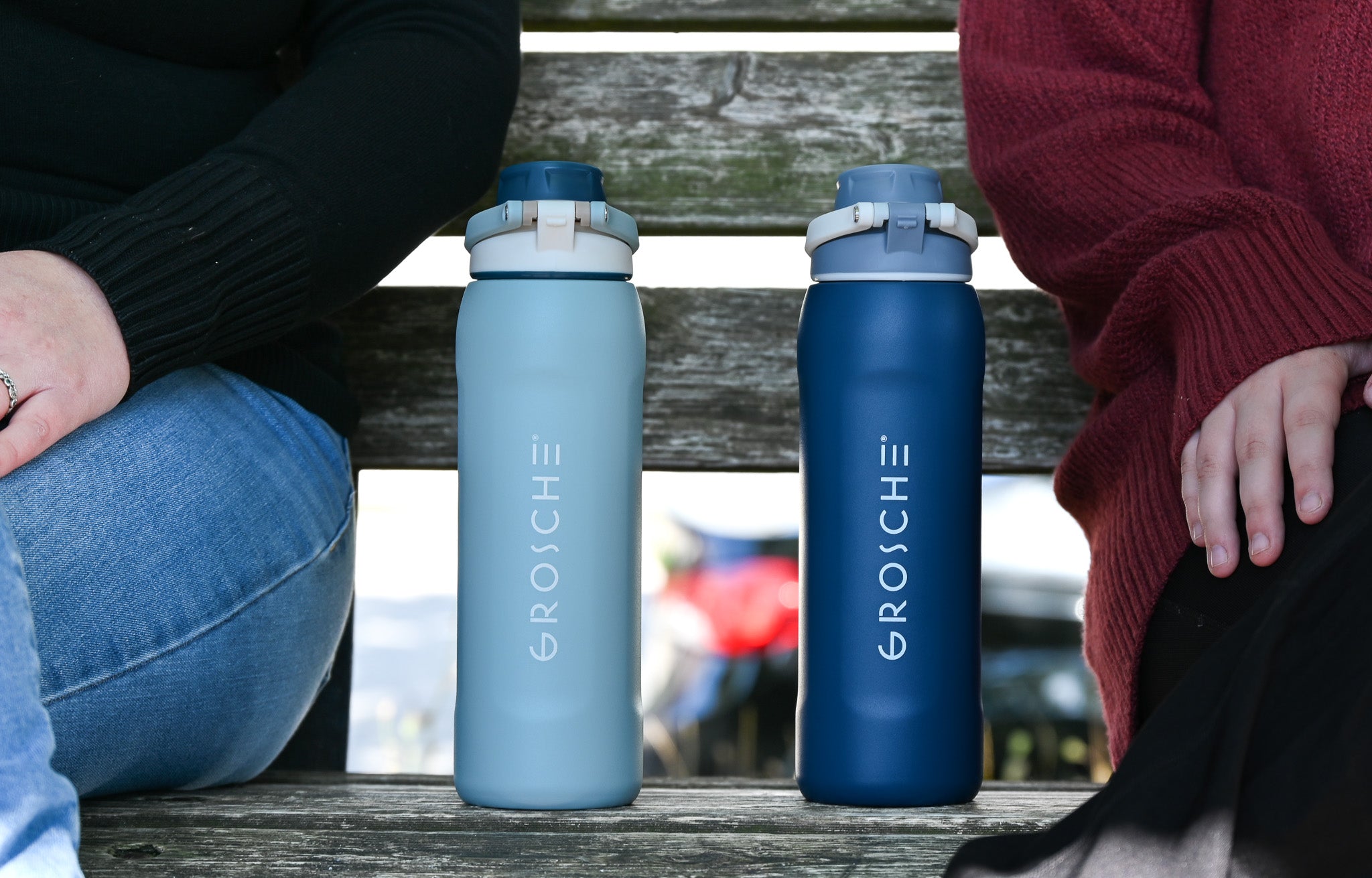 GROSCHE Kamloops Two GROSCHE water bottles on a park bench between two people sitting down.