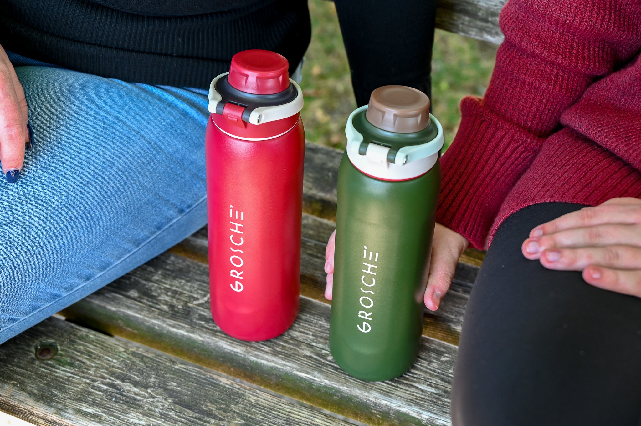 GROSCHE Kamloops Two water bottles, one red and one green, with 'GROSCHE' branding, on a park bench.