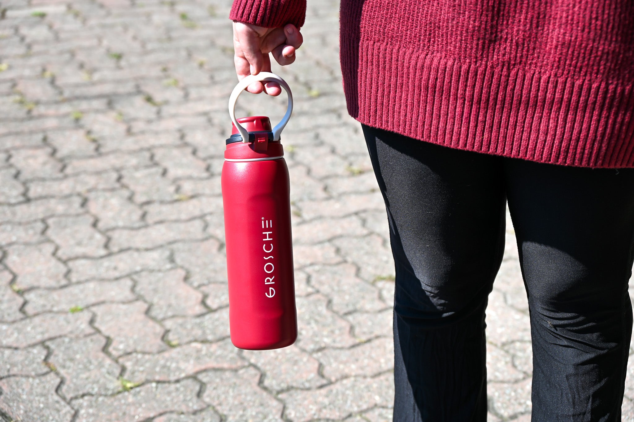 GROSCHE Kamloops Red water bottle with 'GROSCHE' branding held by a person on a paved surface.