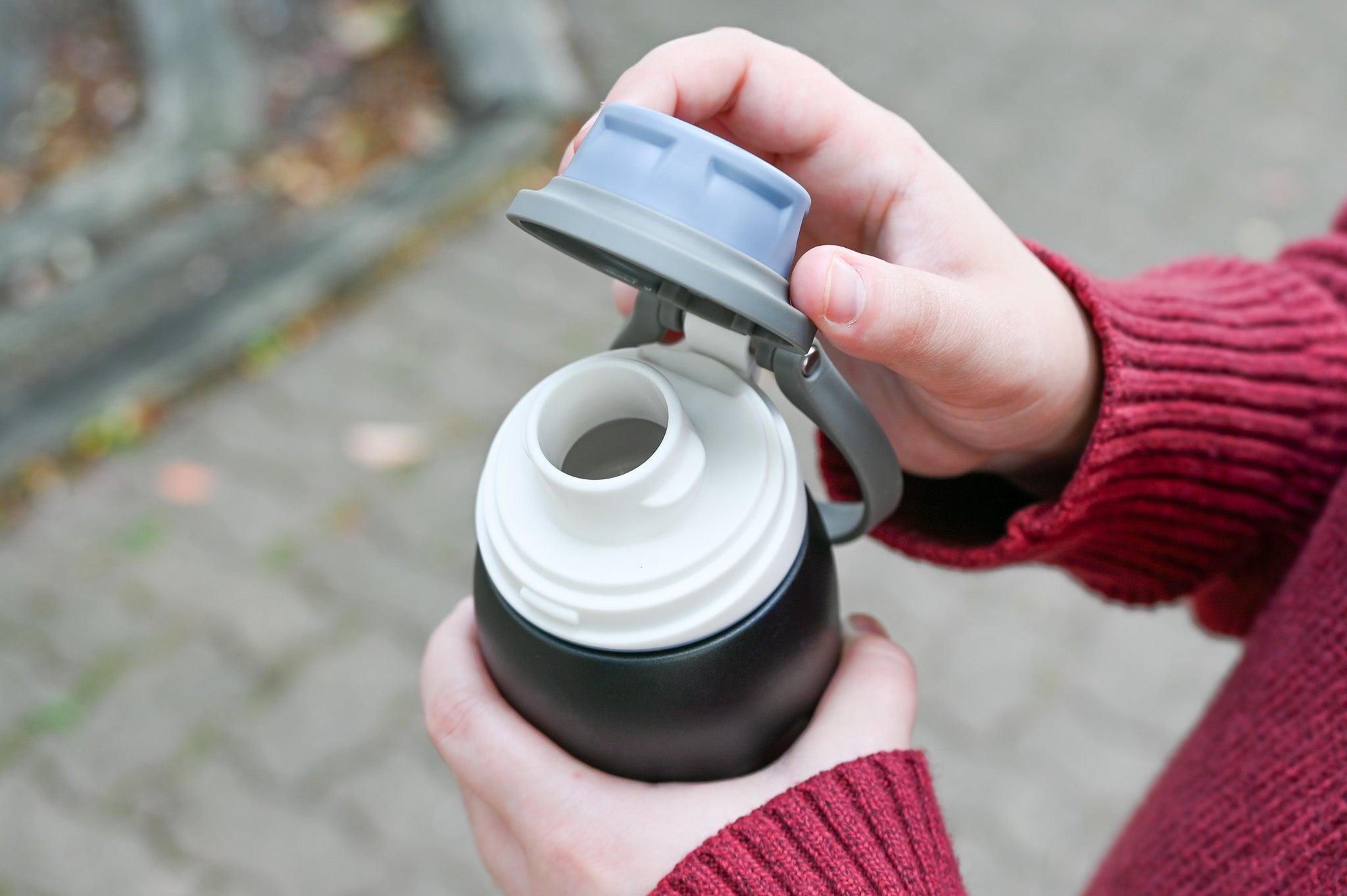 GROSCHE Kamloops Close up of a person's hands holding a black and white water bottle with an open gray lid.