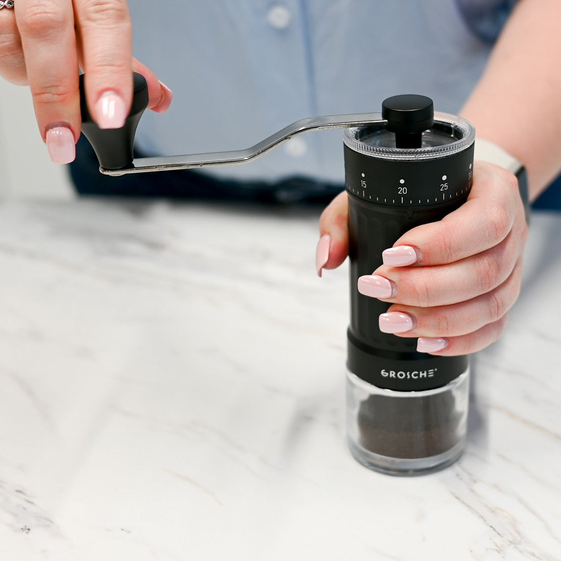 Person using a manual coffee grinder on a light surface