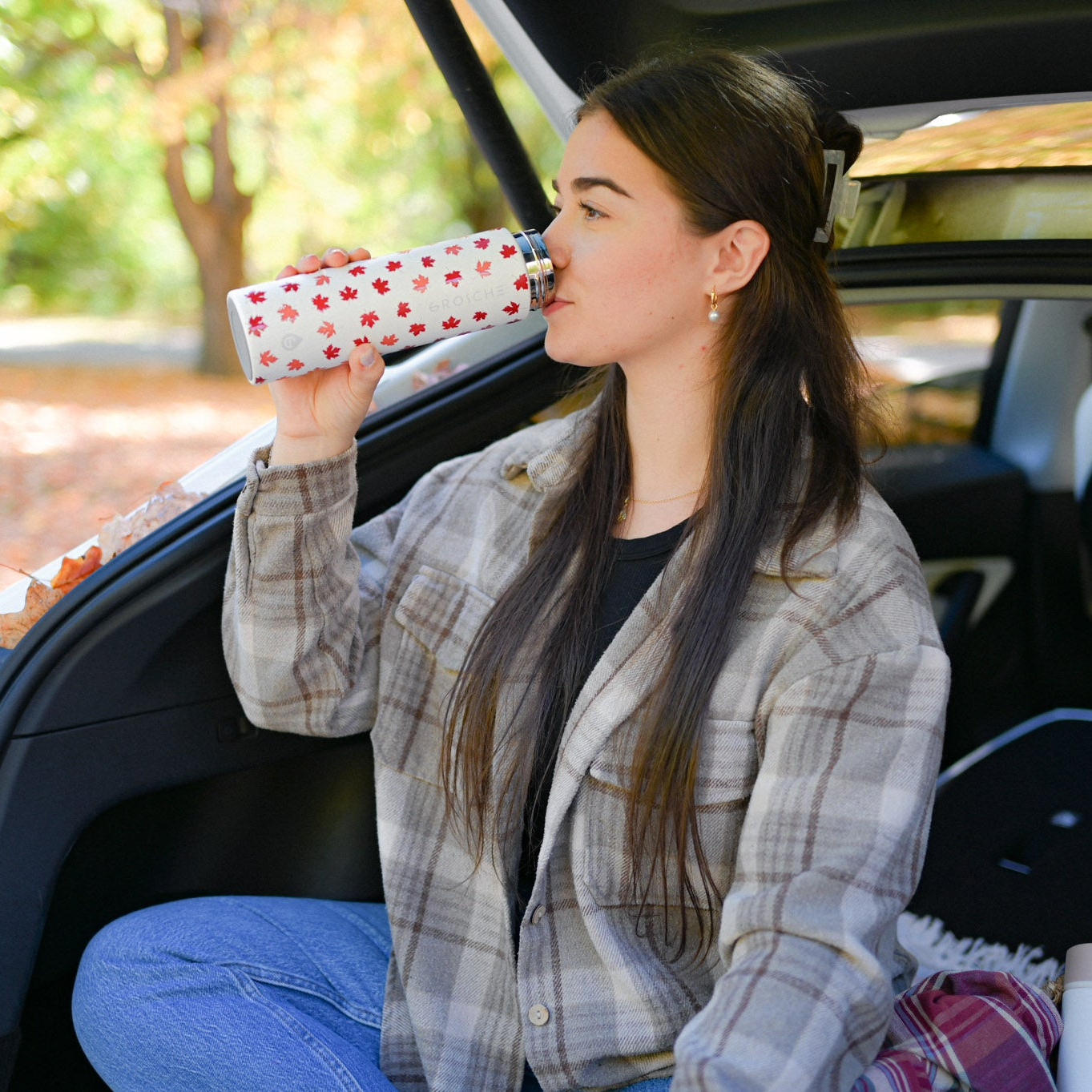 Woman sitting in a car trunk drinking from a maple leaf cup