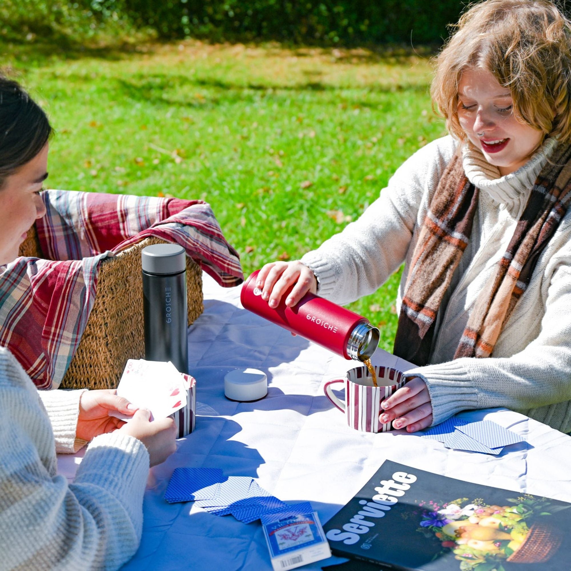 Two women sitting outdoors at a table pouring team from a Toronto tumbler.