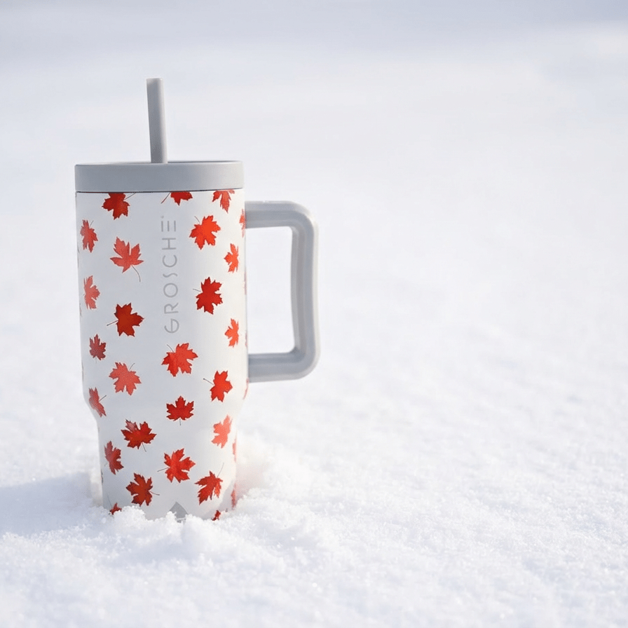 A white GROSCHE Aspen tumbler with red maple leaves decorating the bottle sitting in the snow.
