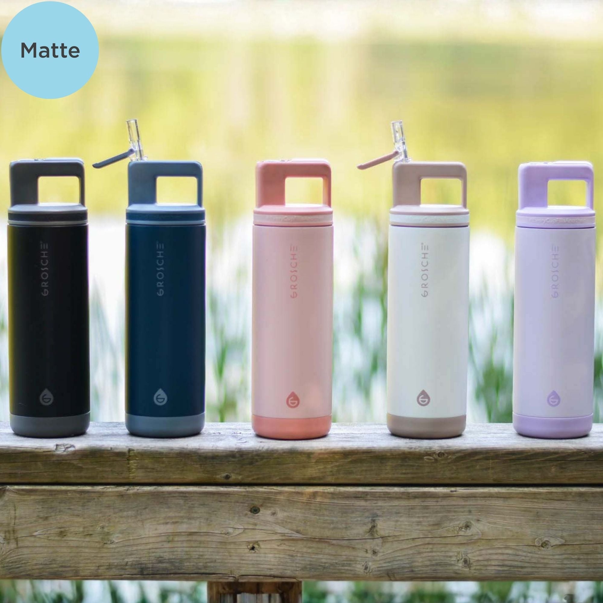 Five insulated bottles with handles and straws on a wooden surface outdoors.
