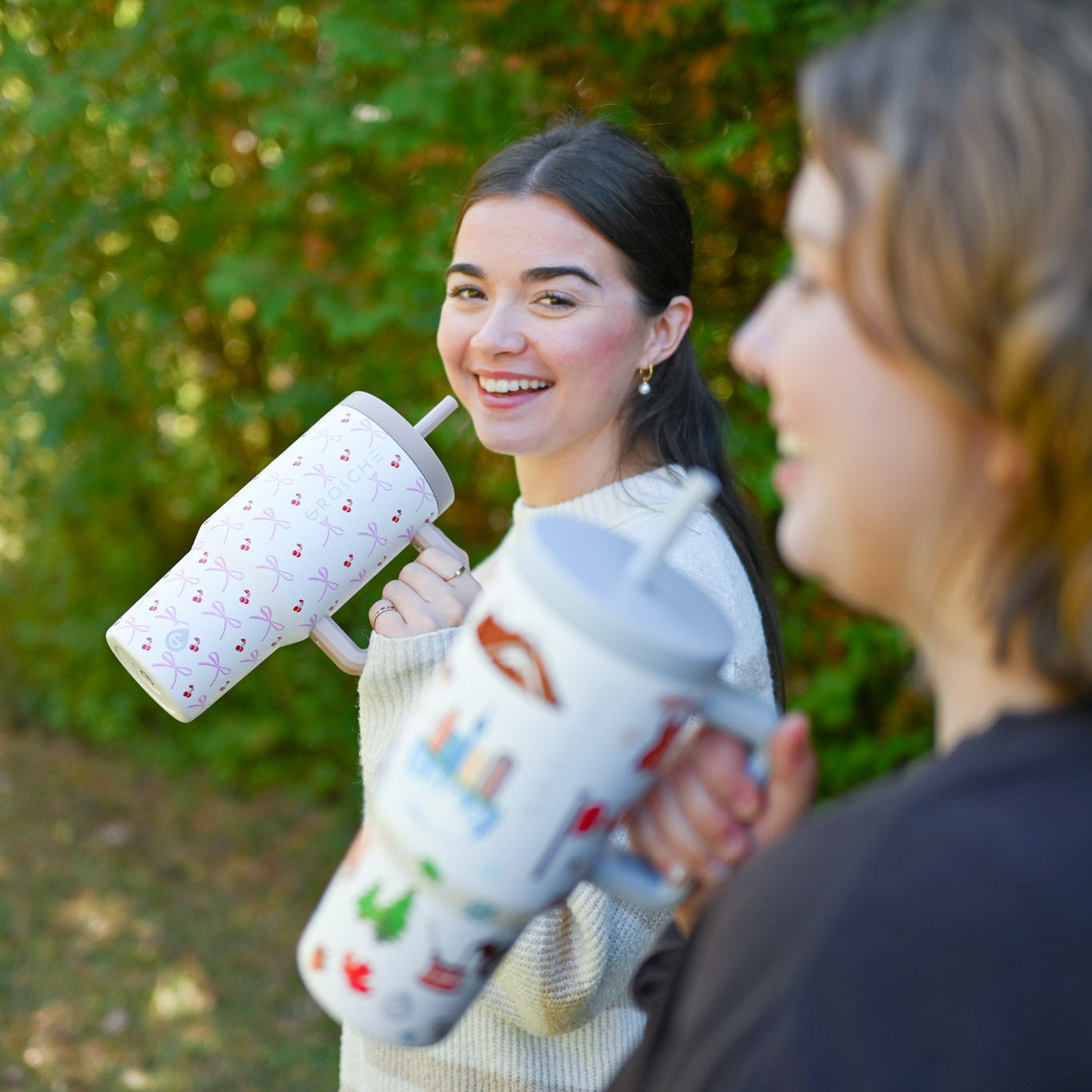 Two people holding colorful water bottles outdoors with greenery in the background