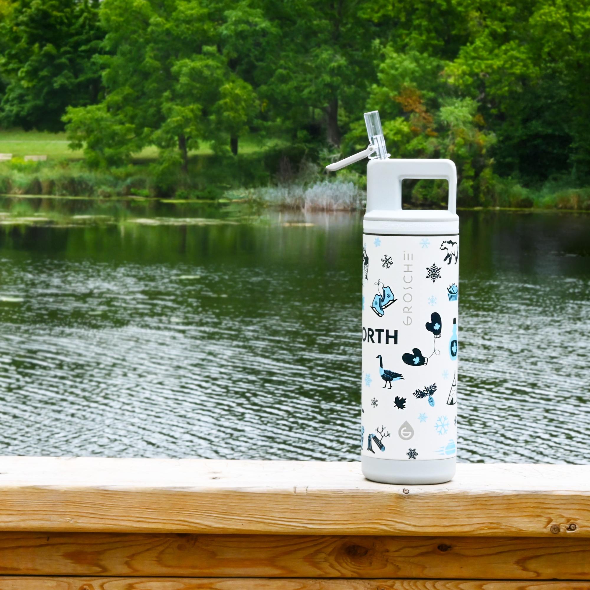 White water bottle with nature-themed design on a wooden ledge by a lake