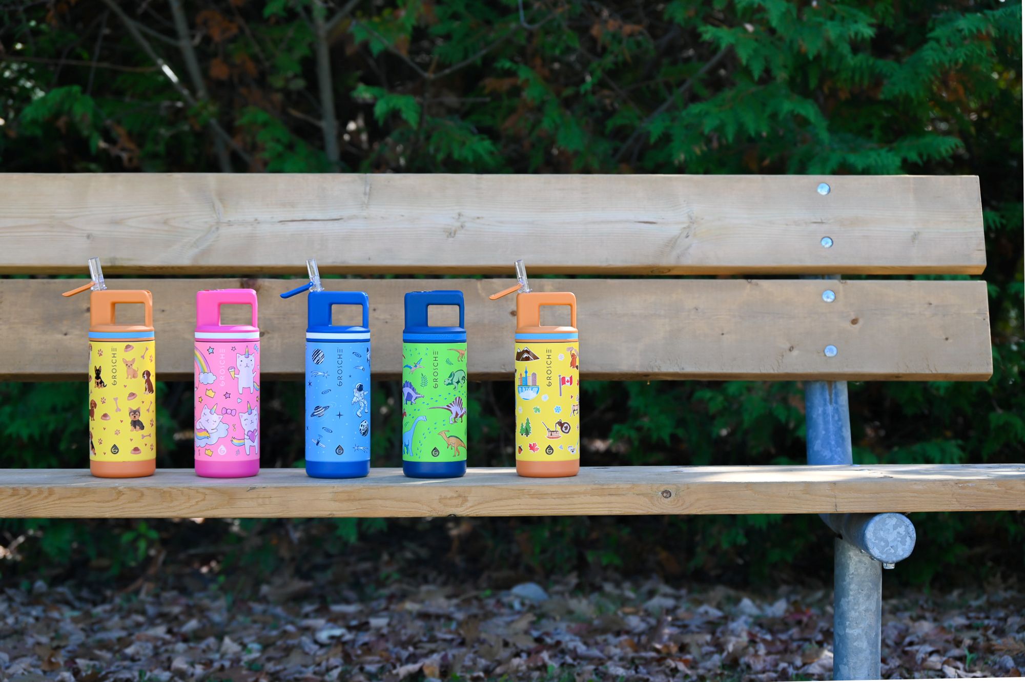 Colorful water bottles with straws on a wooden bench outdoors.