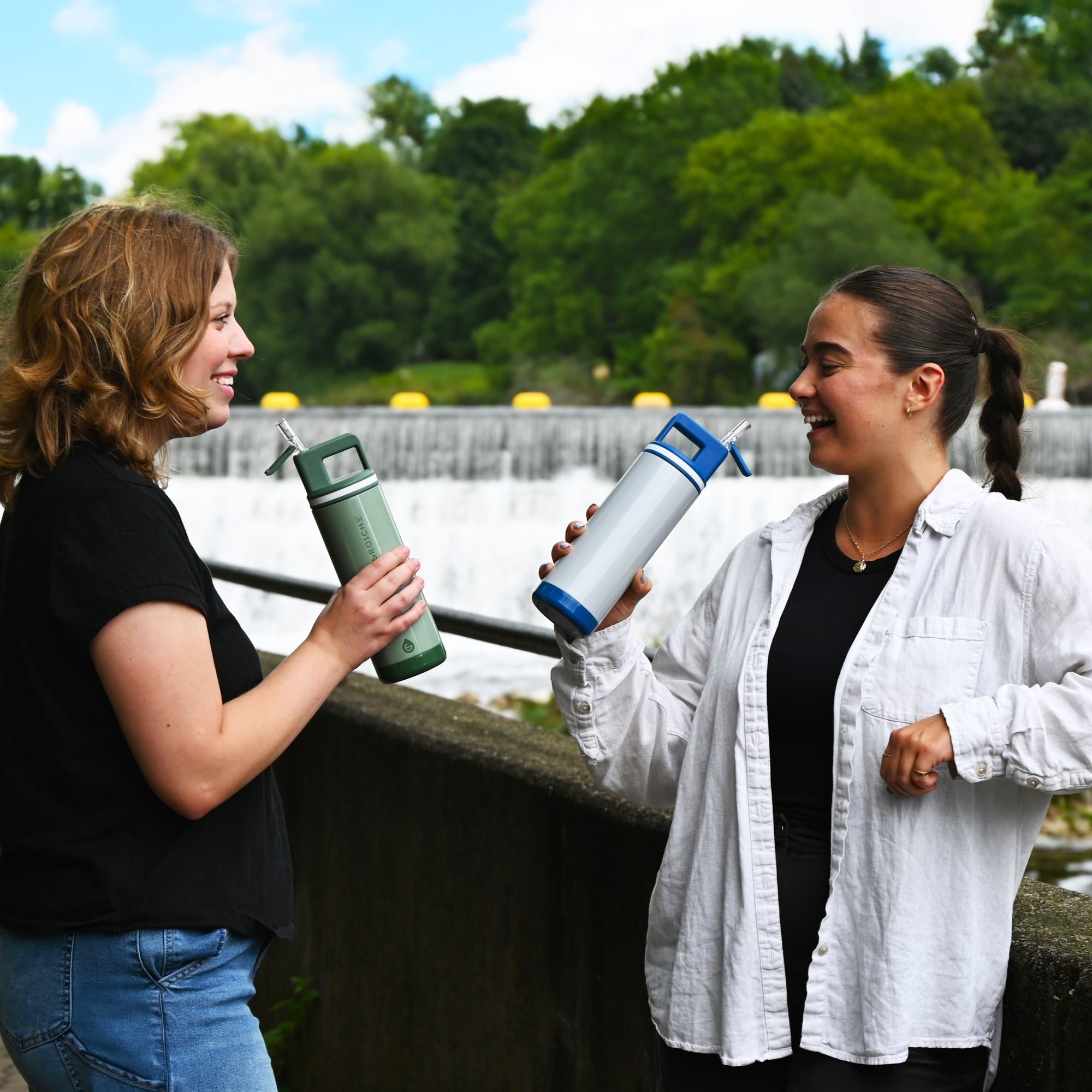 Two women holding water bottles outdoors with a natural background