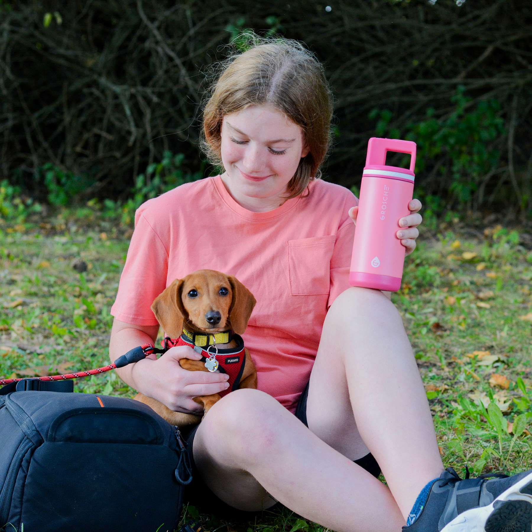 A girl sitting outside with a small dog and holding the Alpine kids water bottle in Flamingo Pink. 