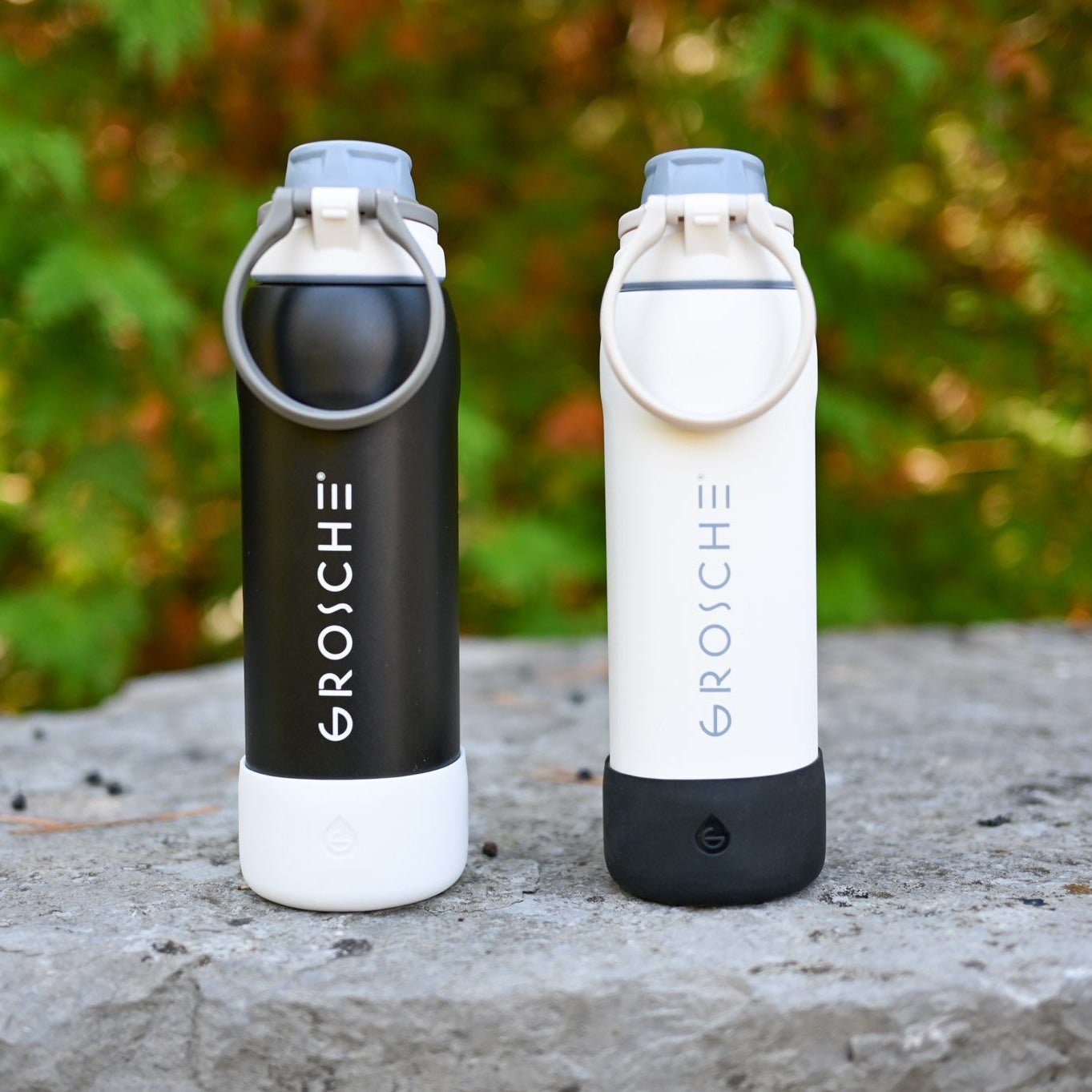 GROSCHE Kamloops  Two GROSCHE bottles, one black and one white, sitting on top of a rock with blurred trees in the background. 