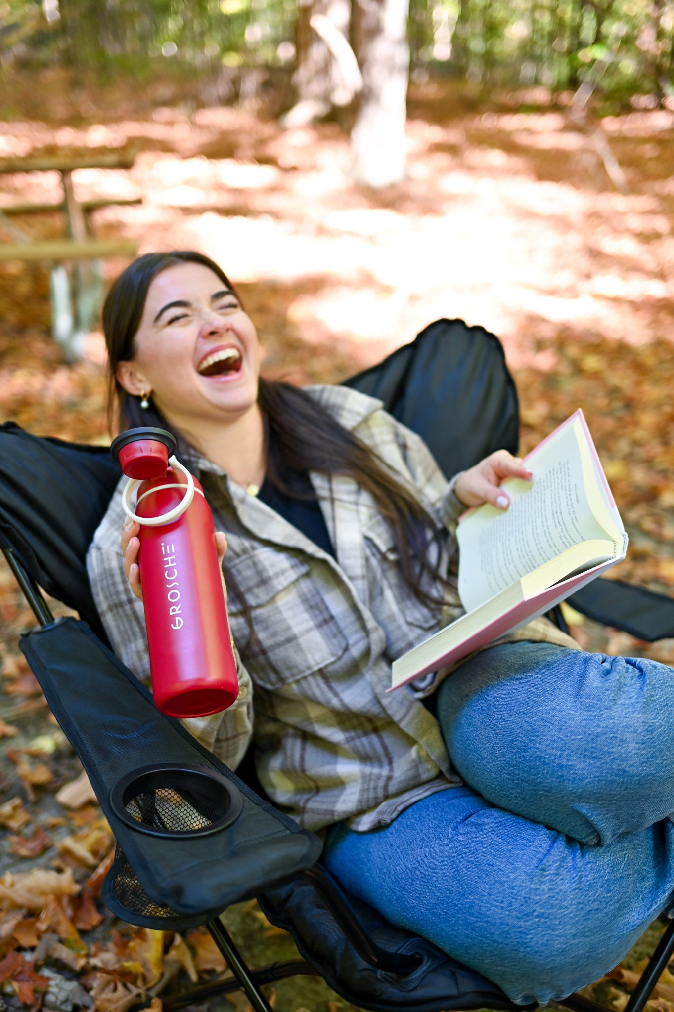 GROSCHE Kamloops  Person sitting outdoors in a chair, laughing and holding an open book and a red water bottle.