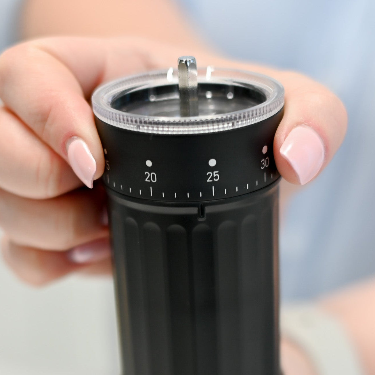 Hand holding a black coffee grinder with a blurred background