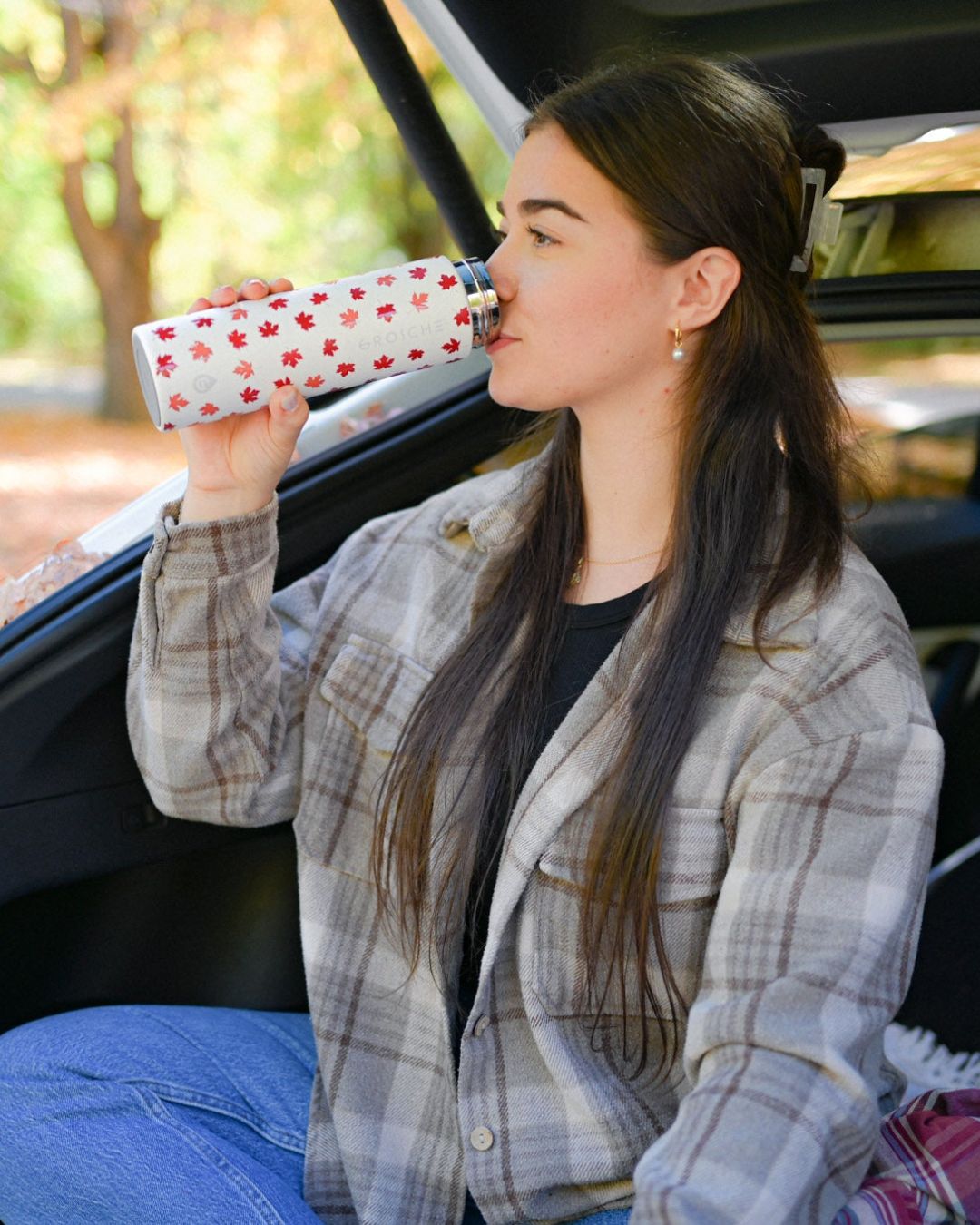 Woman sitting in a car trunk drinking from a maple leaf cup