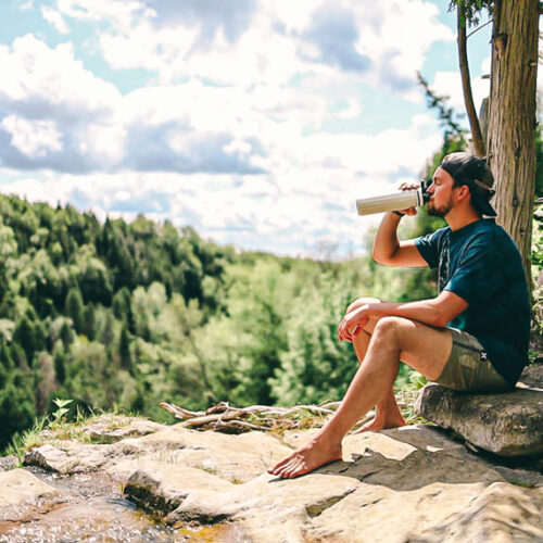 Man drinking from OASIS Infuser Bottle on cliff