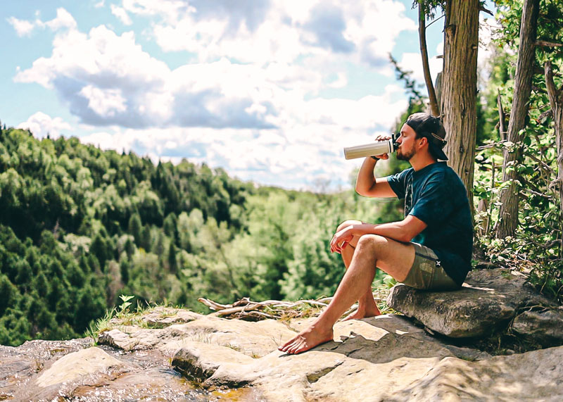 Man drinking from OASIS Infuser Bottle on cliff