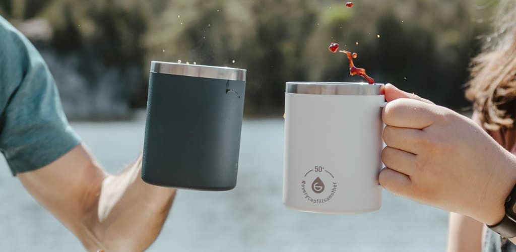 Two people doing a cheers with their EVEREST Insulated Travel Mugs while camping.
